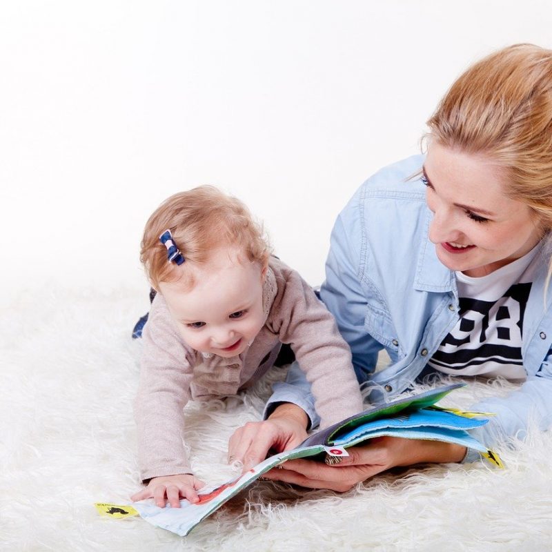 femme et bébé lisant un livre ensemble sur un tapis blanc