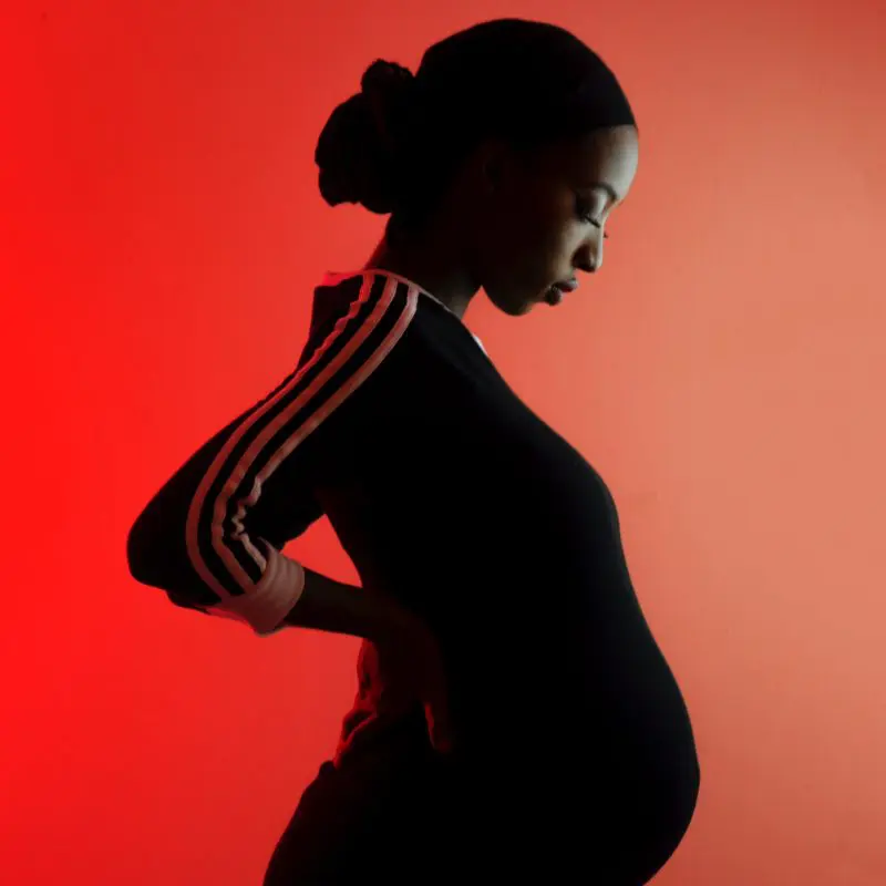 femme enceinte en silhouette portant un vêtement de sport noir sur fond rouge