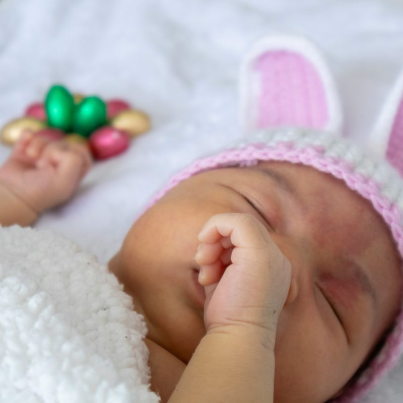 bébé nouveau-né endormi portant un bonnet rose avec des décorations colorées