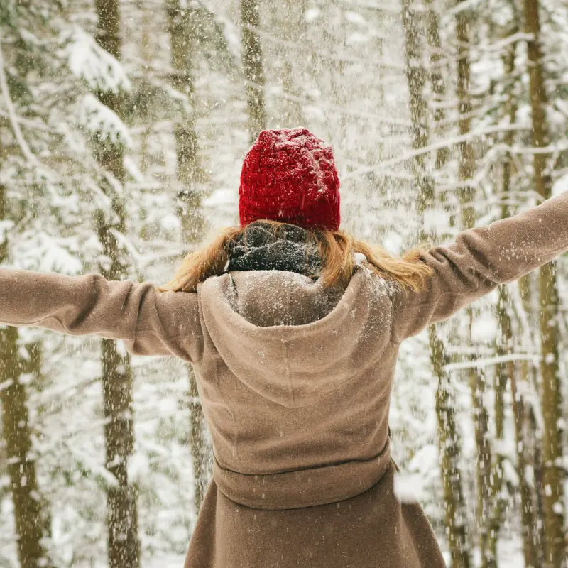 parent célébrant l'hiver dans une forêt enneigée, bras levés vers le ciel