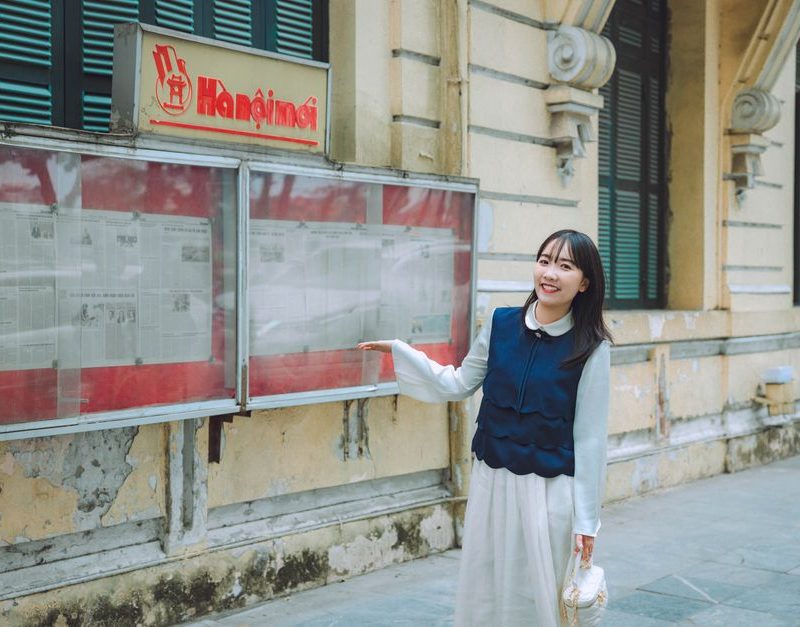 Young woman smiling in front of an outdoor newspaper display.