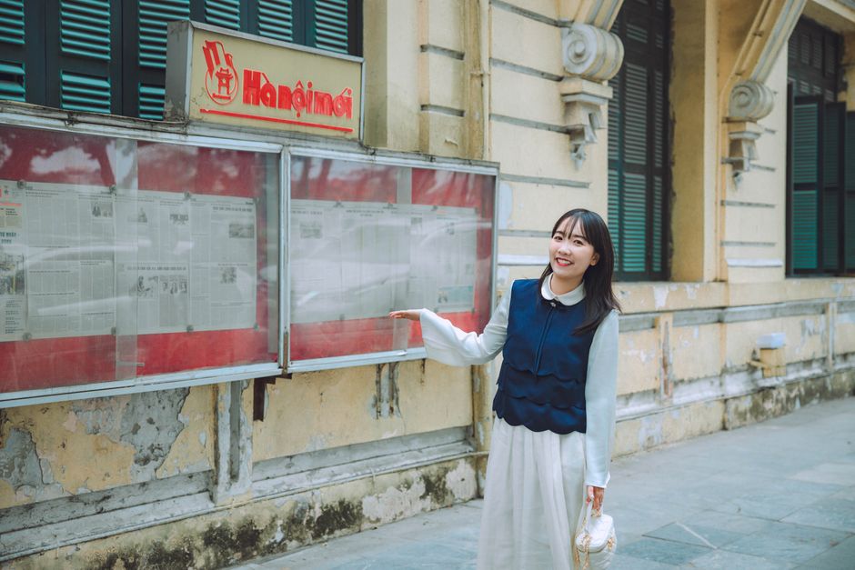 Young woman smiling in front of an outdoor newspaper display.