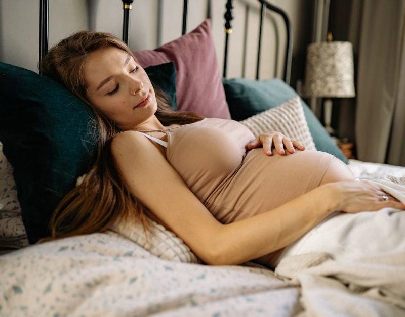 A serene pregnant woman resting in bed, showcasing relaxation and comfort.