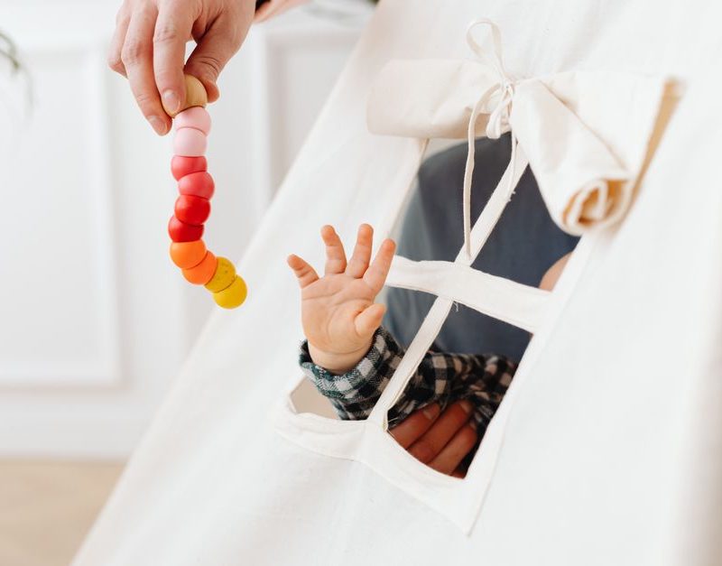 A baby reaches for a colorful toy through a teepee tent window, symbolizing curiosity and play.