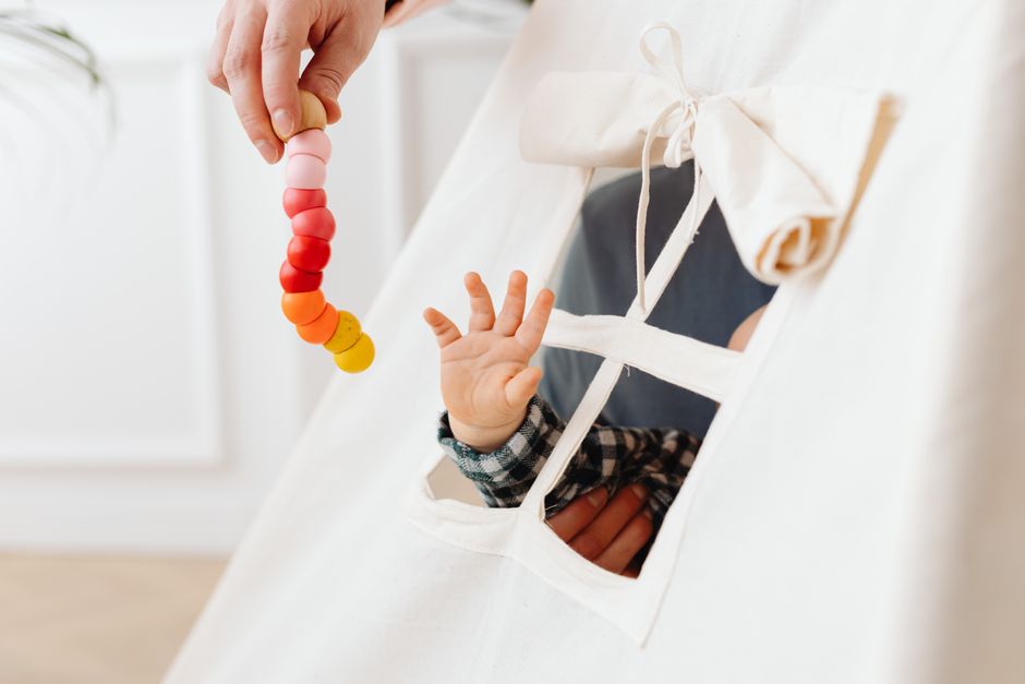 A baby reaches for a colorful toy through a teepee tent window, symbolizing curiosity and play.