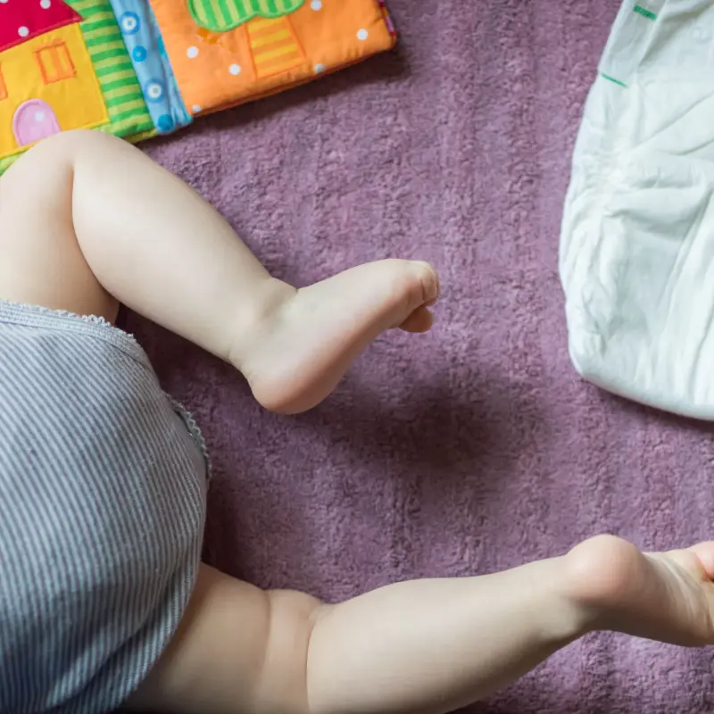bébé en couche écologique sur tapis violet avec jouets colorés
