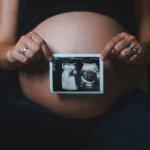 a pregnant woman holding a camera in her hands